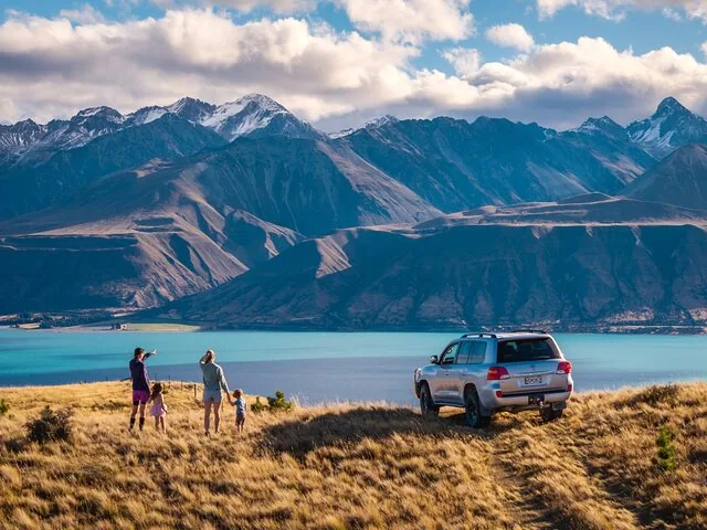 Family standing near a parked SUV overlooking a stunning blue lake