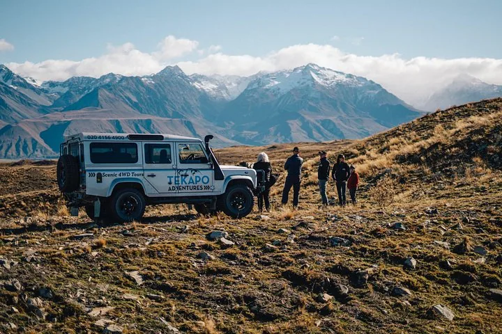 Eine Gruppe von Personen steht neben einem weißen 4WD-Fahrzeug in einer Berglandschaft.