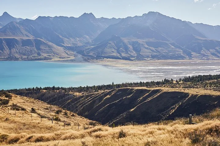Scenic view of a bright blue lake surrounded by golden hills and mountains.