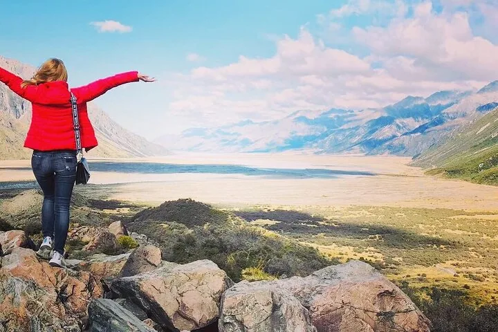 Person in roter Jacke steht auf Felsen und blickt über ein weites Tal